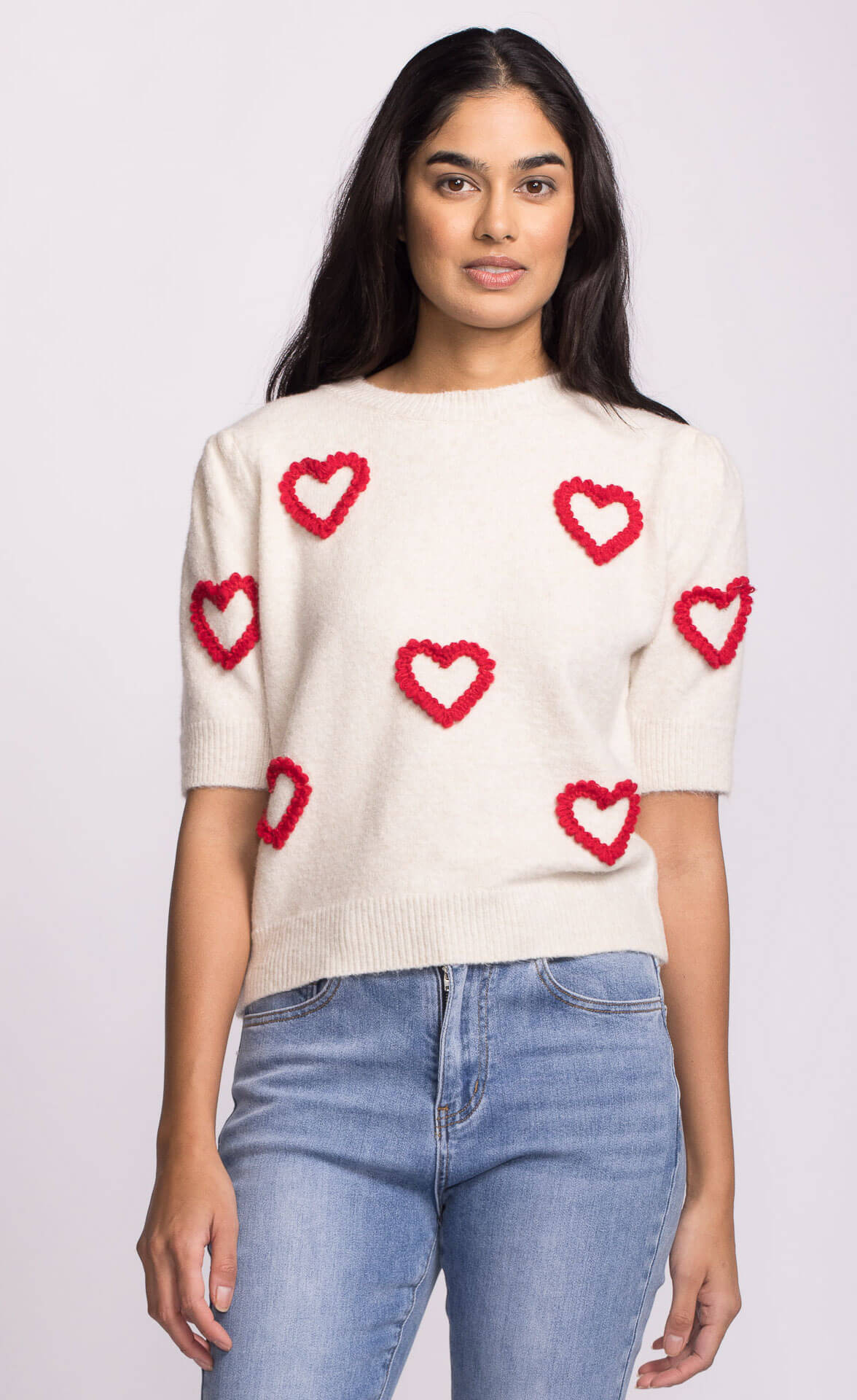 Close-up of ivory sweater showing playful red heart accents on body and sleeves.