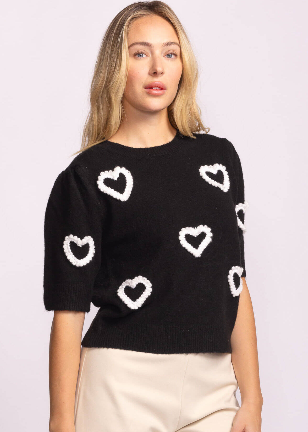 Three-quarter angle showing black sweater with scattered white hearts.