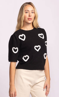 Three-quarter angle showing black sweater with scattered white hearts.