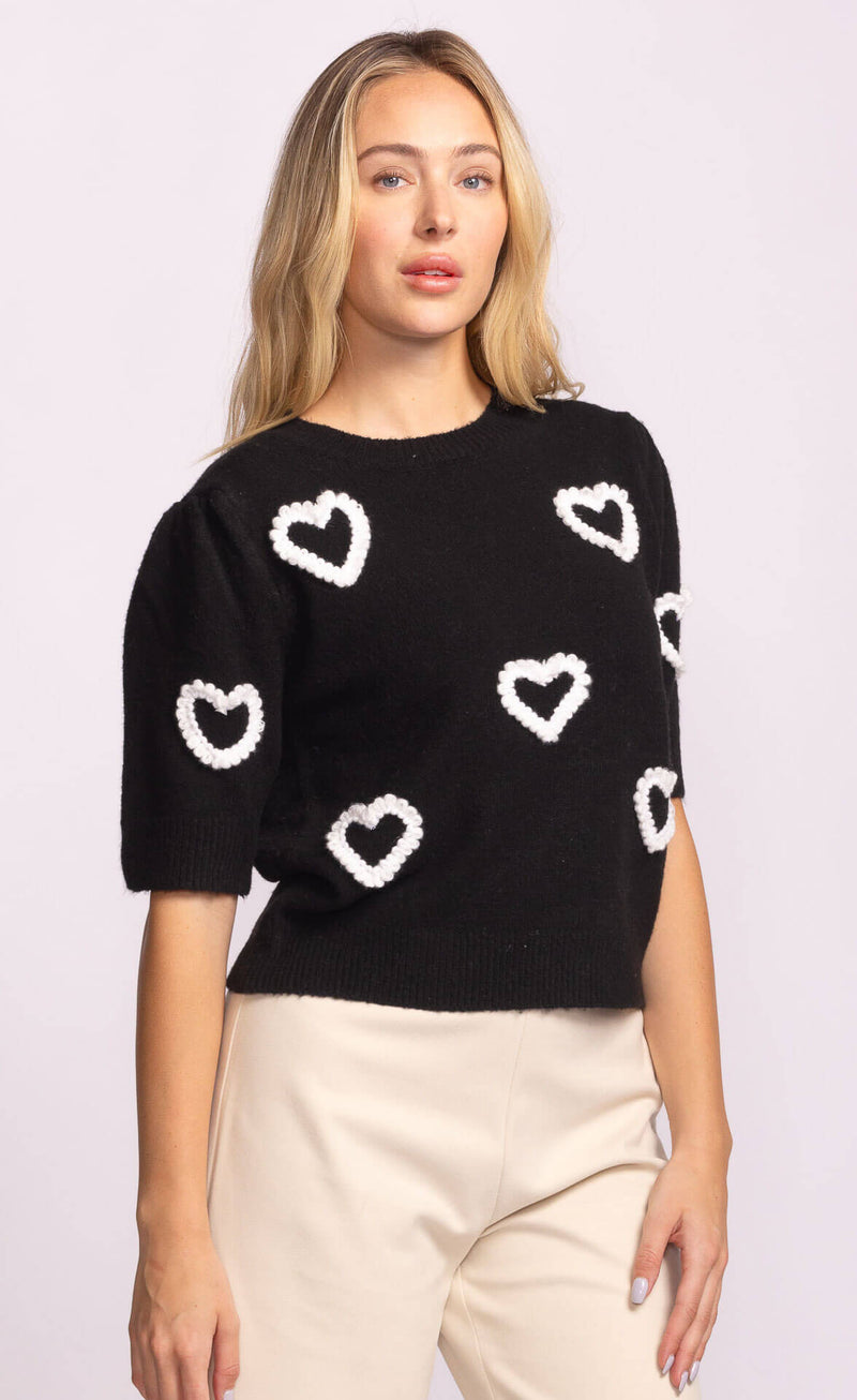 Three-quarter angle showing black sweater with scattered white hearts.