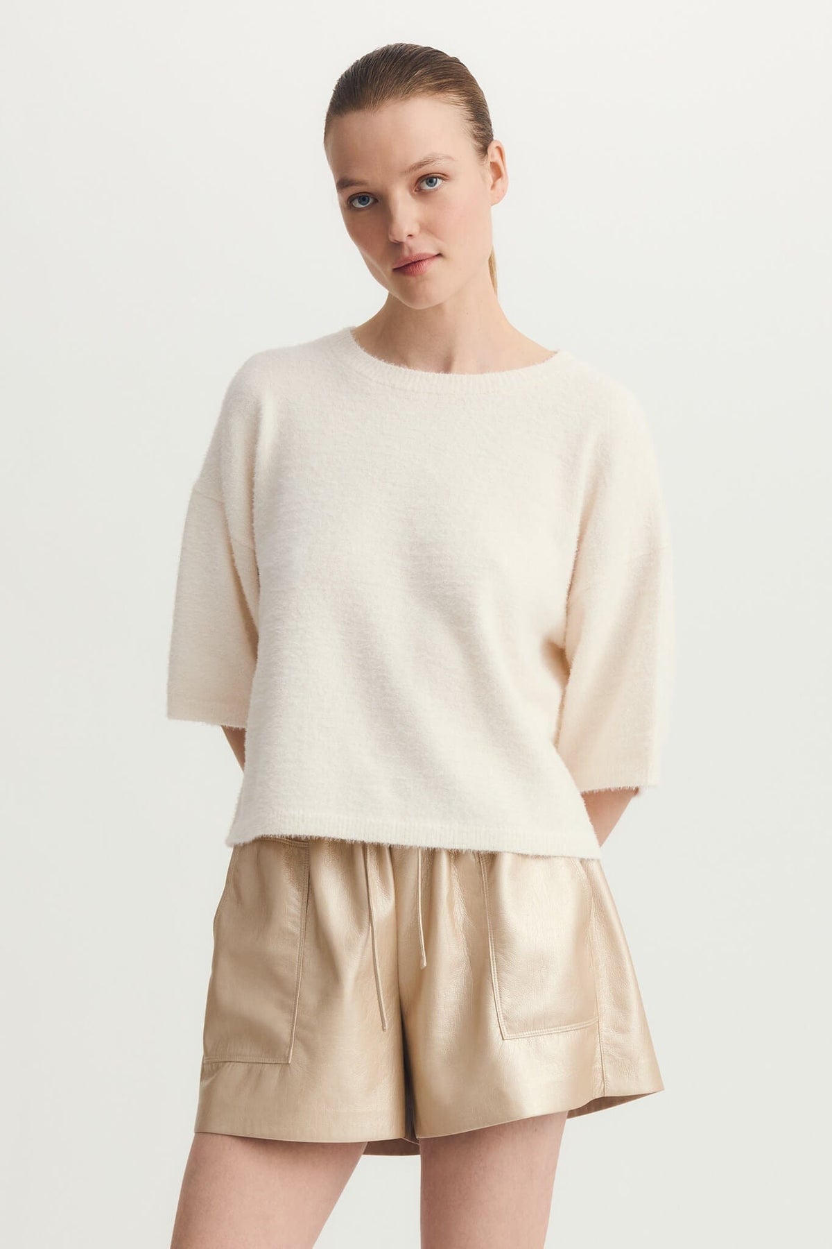 Model wearing Melissa Nepton Jenna Sweater in Off-White with beige shorts, front view, minimal background