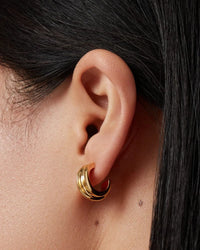 Close-up of an ear wearing Jenny Bird Mini Lennon gold hoop earrings with dark hair partially covering the frame.