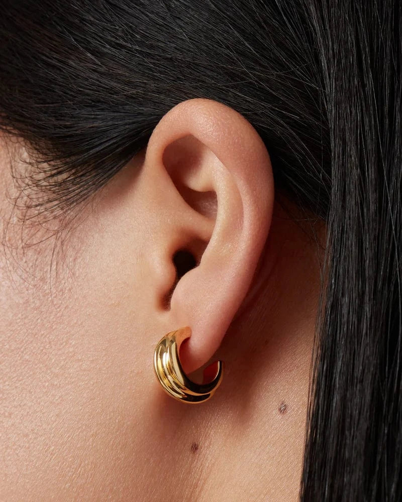 Close-up of an ear wearing Jenny Bird Mini Lennon gold hoop earrings with dark hair partially covering the frame.