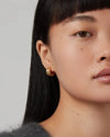 Close-up of a person wearing Jenny Bird Mini Lennon gold hoop earrings with a neutral background