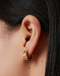 Close-up of an ear wearing Jenny Bird Mini Lennon gold hoop earrings with dark hair partially covering the frame.