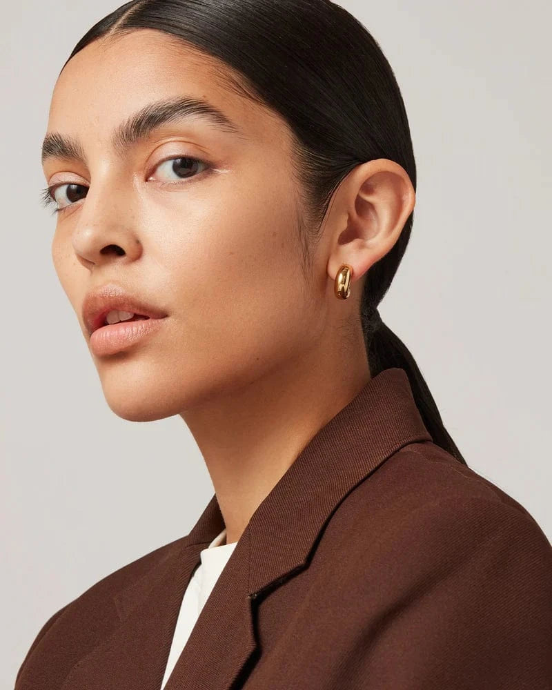 Woman wearing a gold earring with a plain background