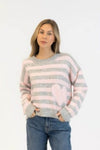 Model wearing grey and pink striped pullover with soft pink heart, styled with denim