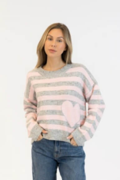 Model wearing grey and pink striped pullover with soft pink heart, styled with denim