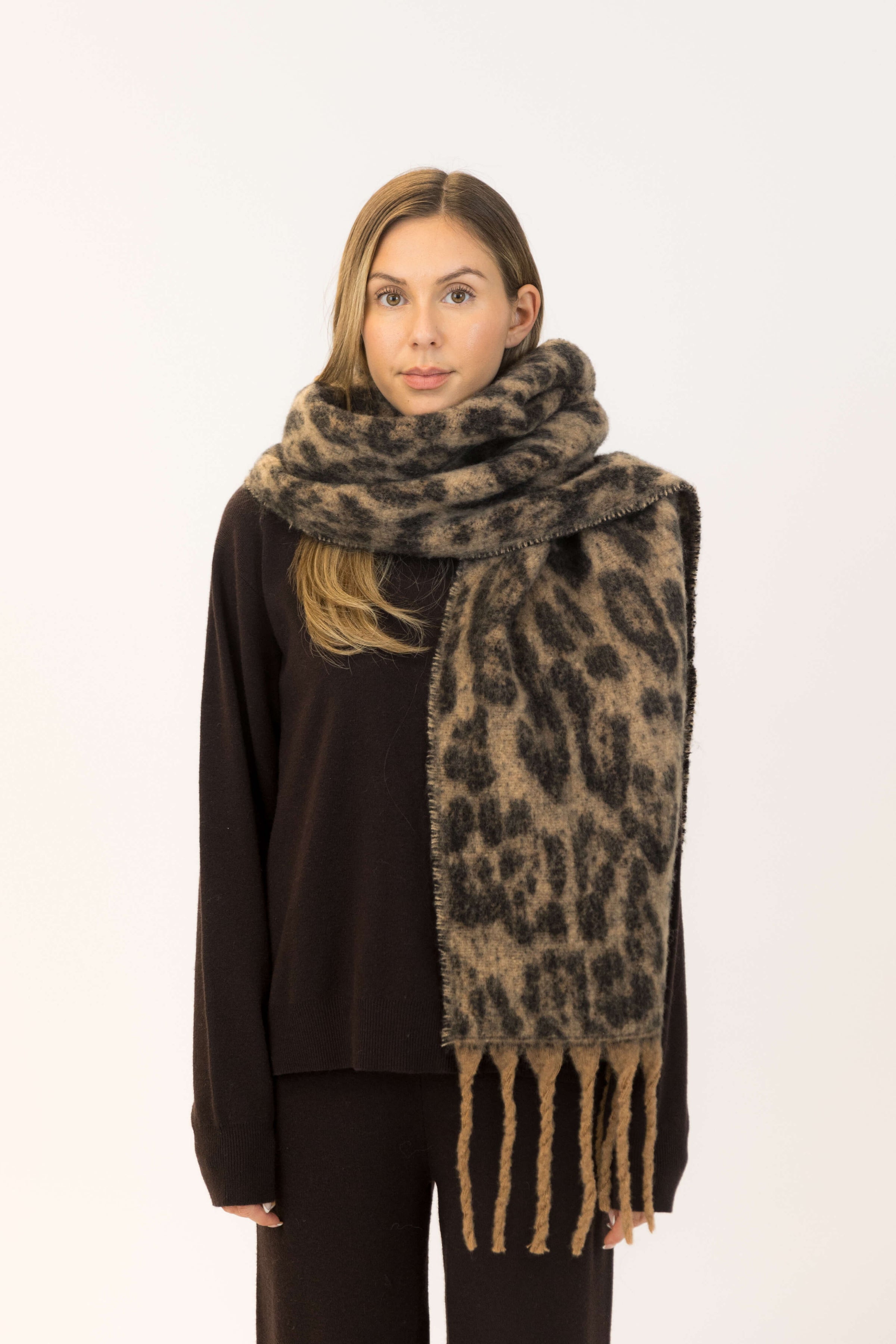 Model wearing Lyla & Luxe Leo Scarf in camel and black leopard print with oversized fringe, styled with a black sweater at Lemonberry.