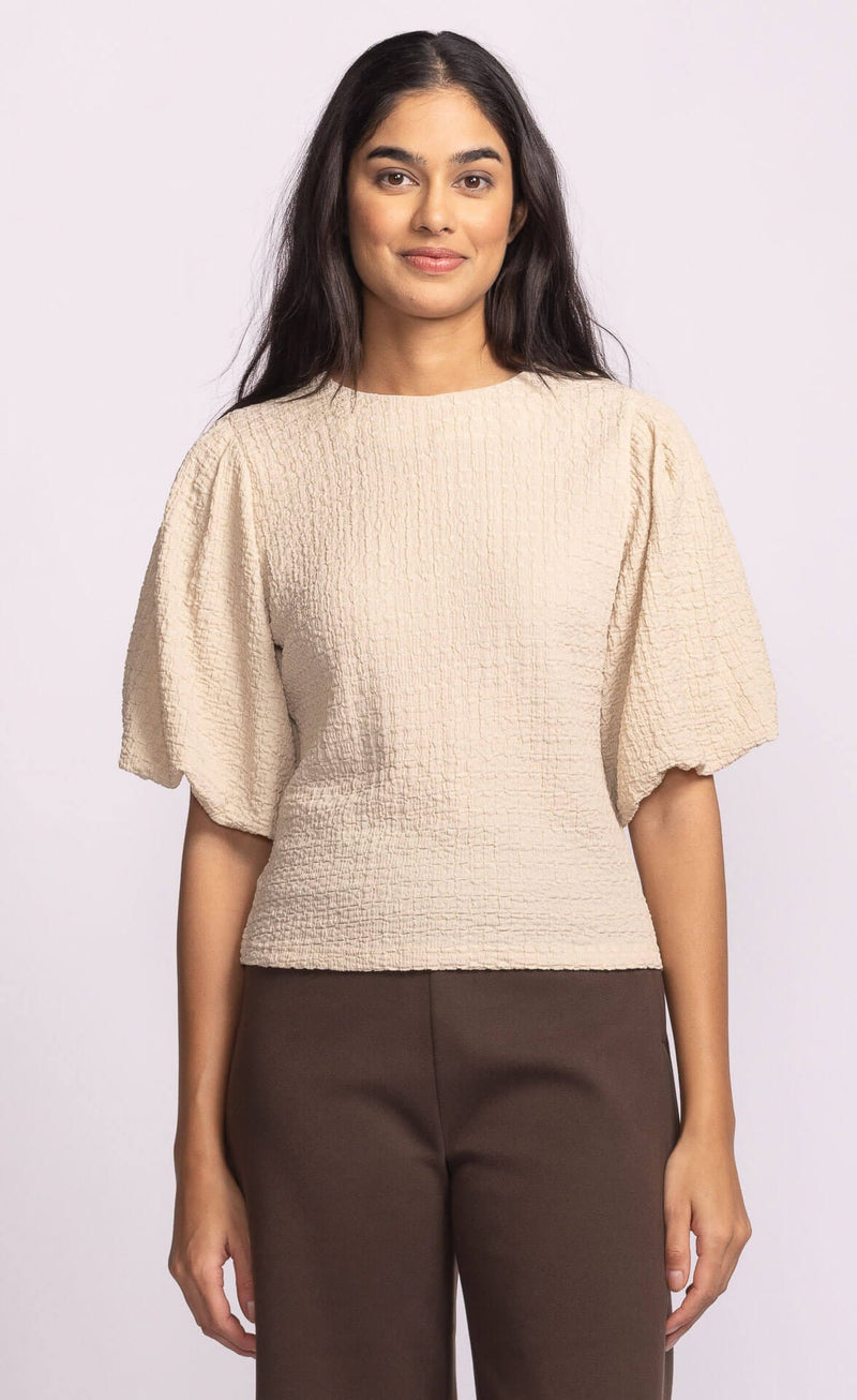 Model wearing Pink Martini Lita Top in beige with puff sleeves, front view.