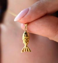 Gold fish-shaped pendant held by a hand against a blurred background