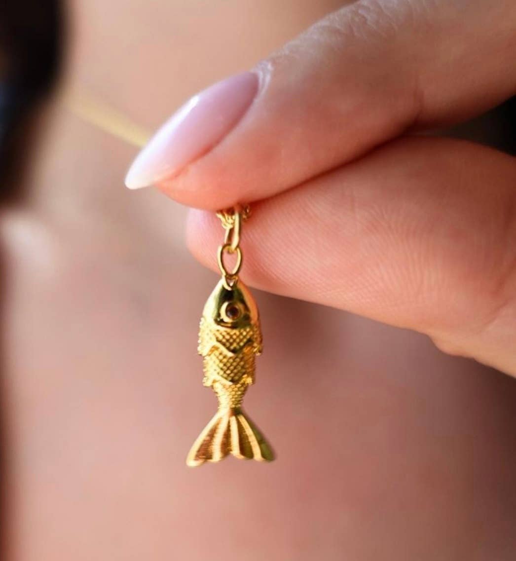 Gold fish-shaped pendant held by a hand against a blurred background