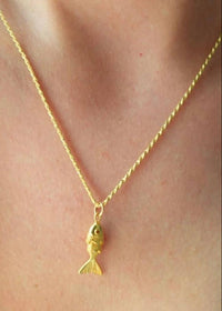 Gold fish-shaped pendant necklace on a person's neck
