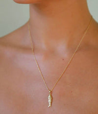Gold necklace with a leaf-shaped pendant on a person's neck