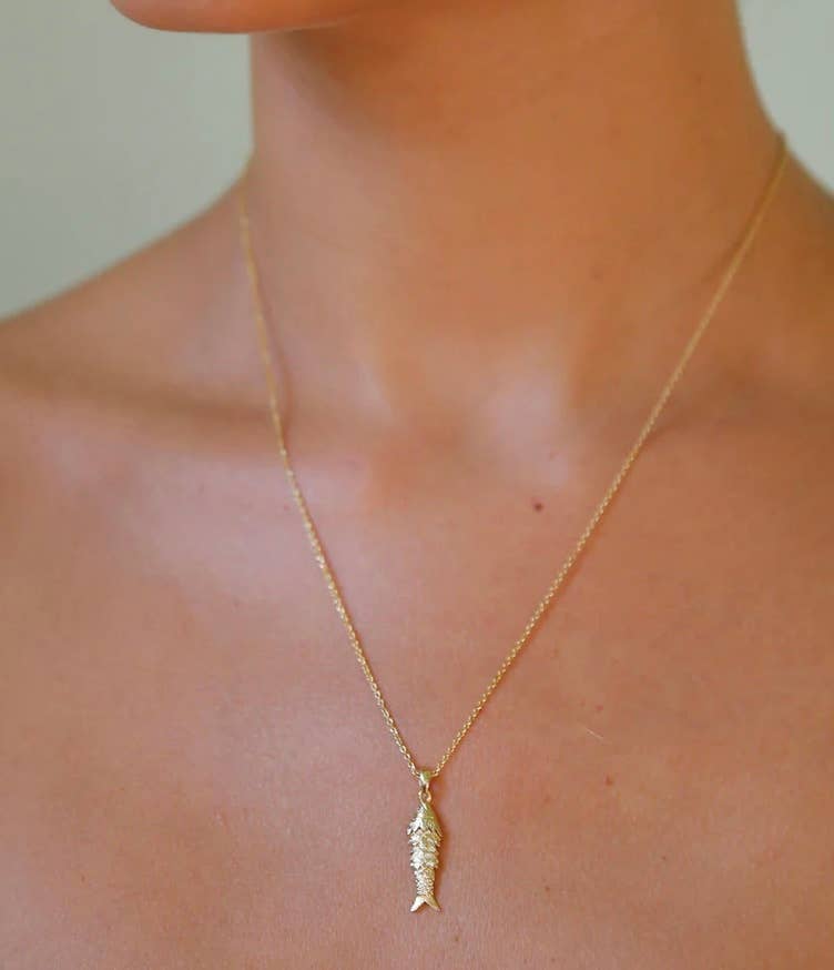 Gold necklace with a leaf-shaped pendant on a person's neck