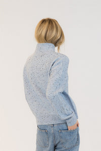Back view of a person wearing a light blue speckled sweater and jeans on a plain background at Lemonberry in Aurora, Ontario