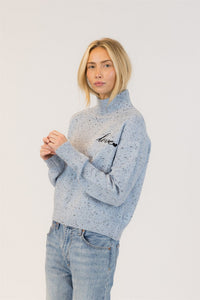 Side view of a woman wearing a light blue sweater with 'love' embroidery on a white background