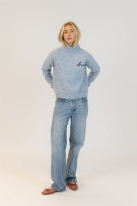 Person wearing a light blue turtleneck sweater by Lyla & Luxe with jeans on a white background