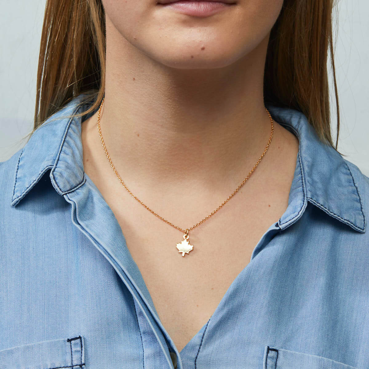 Maple Leaf Charm Necklace by Foxy Originals in gold, styled on model in chambray shirt