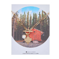 Gold Maple Leaf Toggle Necklace with pearl charm – displayed on card packaging with forest cabin design