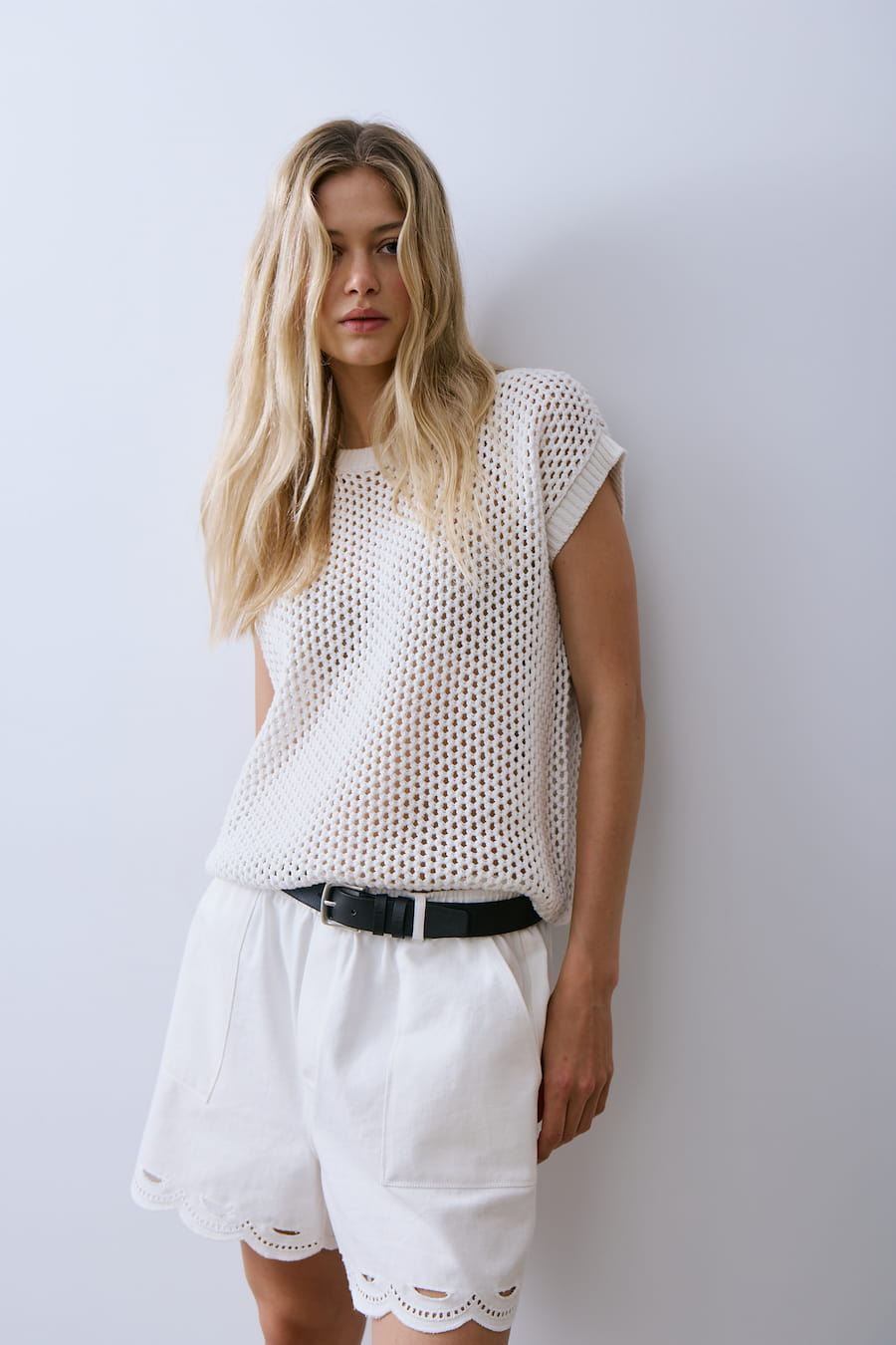 Woman wearing a white sleeveless top and shorts against a plain background