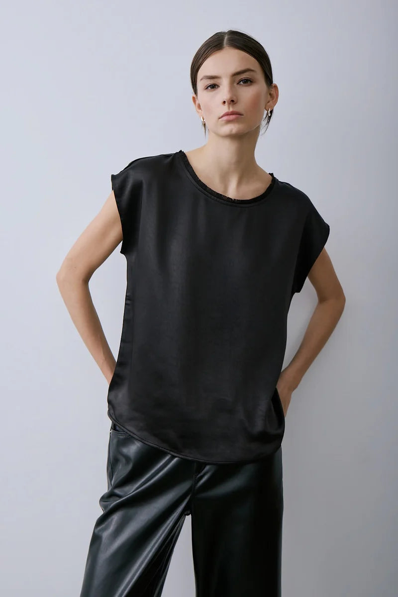 Person wearing a black sleeveless Willow Top by Melissa Nepton and black pants against a light grey background.
