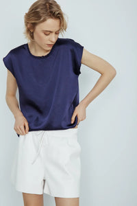 Person wearing a navy sleeveless Willow top by Melissa Nepton and white shorts on a light gray background