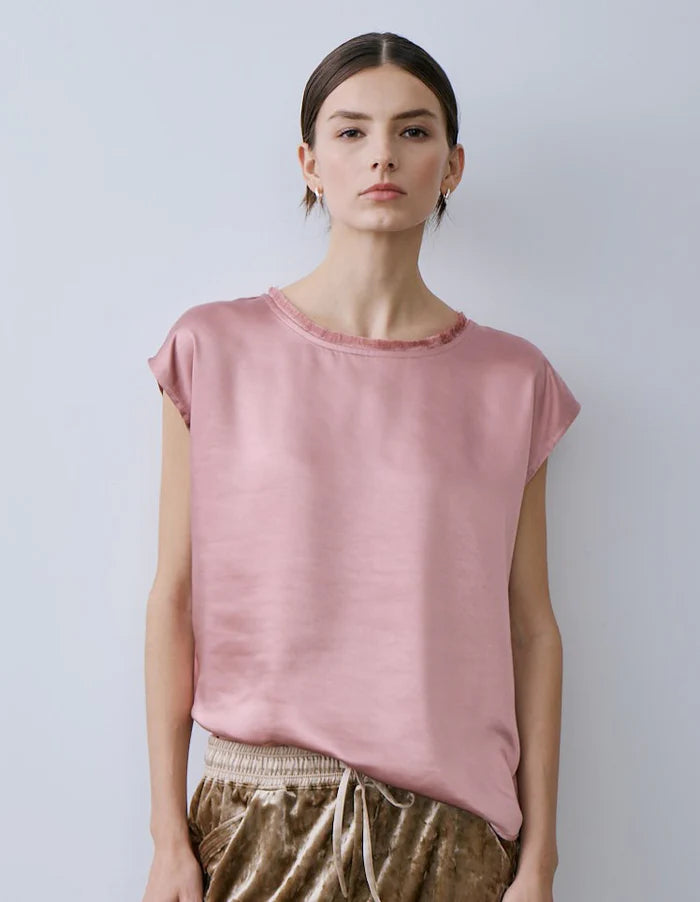 Woman wearing a pink Willow top bgy Melissa Nepton and brown pants against a plain background