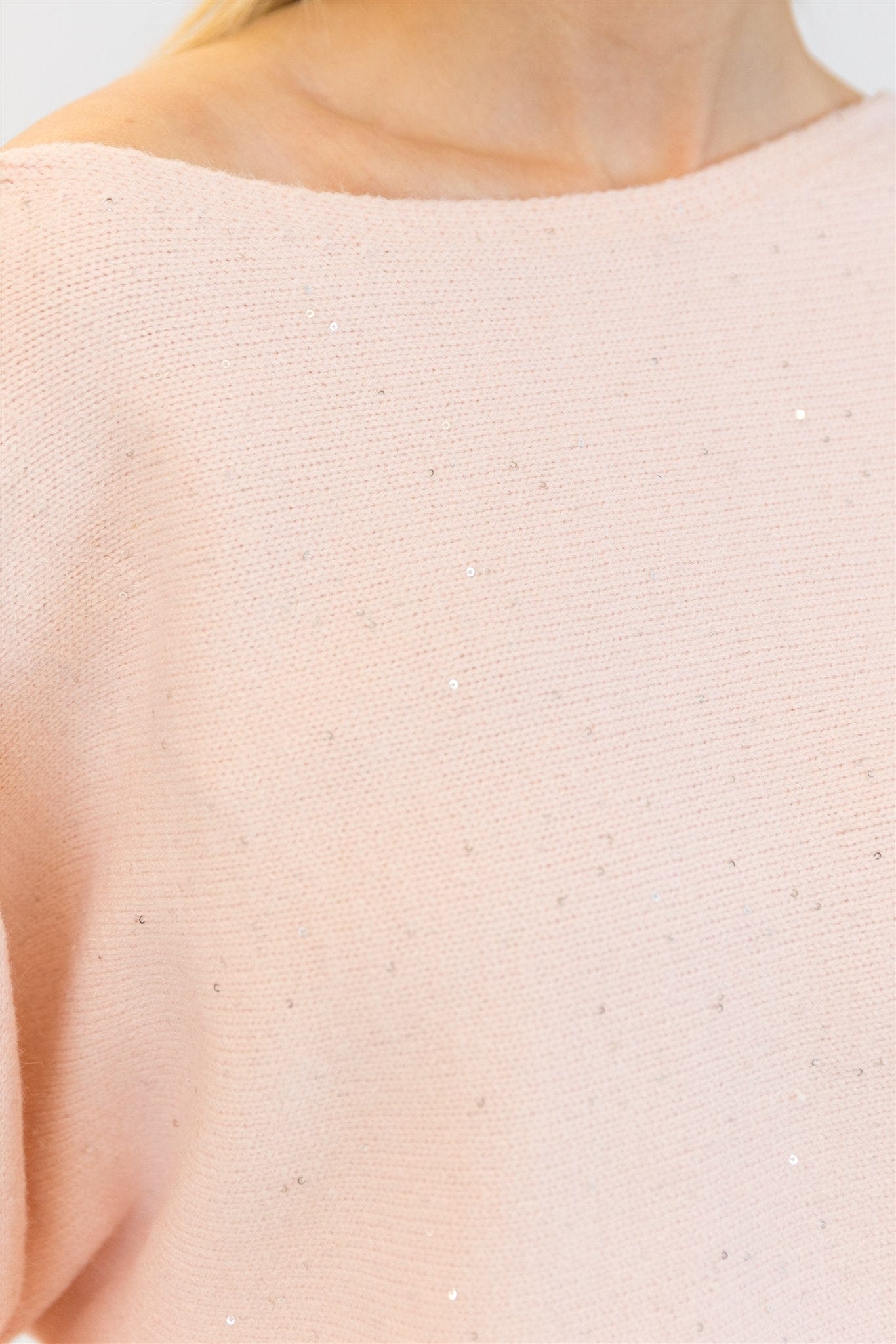 Close-up of sweater fabric showing pale pink knit and scattered sequin detail.