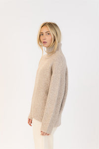 Side view of mockneck sweater in oat, styled with soft waves and minimalist cords