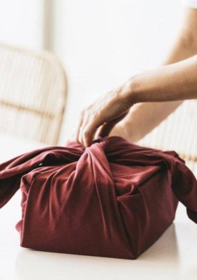 Olsen + Olsen Furoshiki wrap in red flannel – hand tying scene, Lemonberry Aurora, sustainable gift idea.