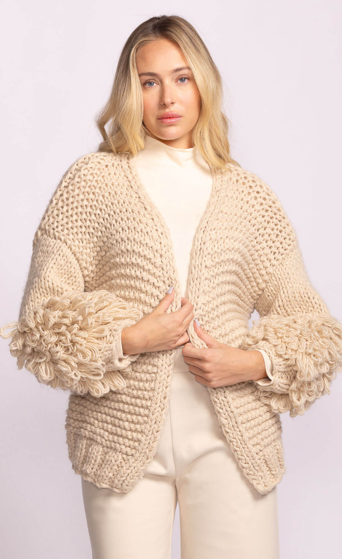 Side view of Palermo Sweater by Pink Martini in cream, featuring oversized looped sleeves and chunky knit texture – Lemonberry boutique.