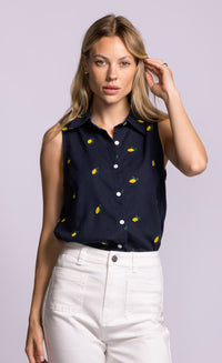 Woman wearing a Pink Martini navy sleeveless shirt with yellow patterns and white pants on a light purple background