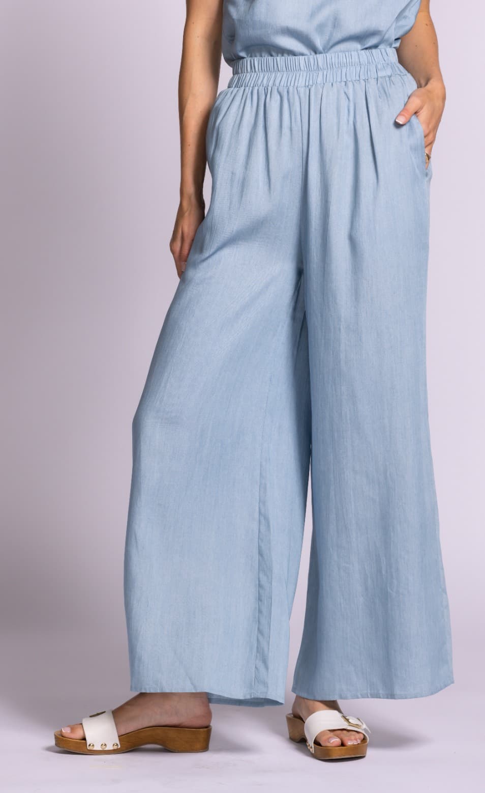 Angled front view of Pink Martini Dash blue wide-leg pants styled with wooden sandals