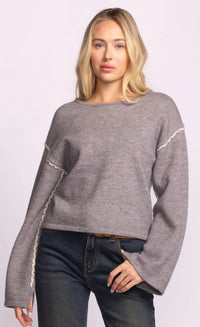 Woman wearing a gray Grenola sweater by Pink Martini with white trim on a light purple background