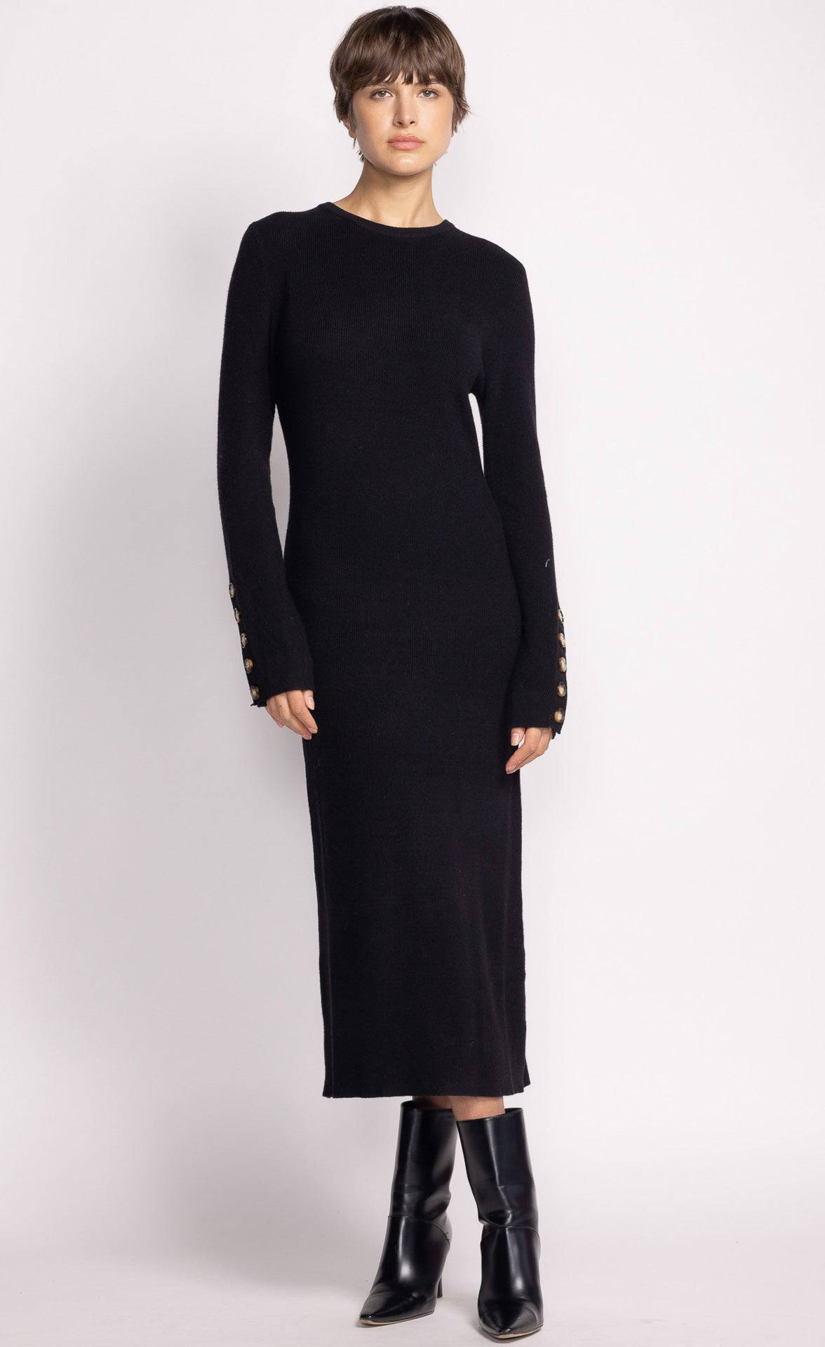 A model wearing a blackPink Martini Harley dress with a crew neck and button details at the cuffs, paired with black boots.