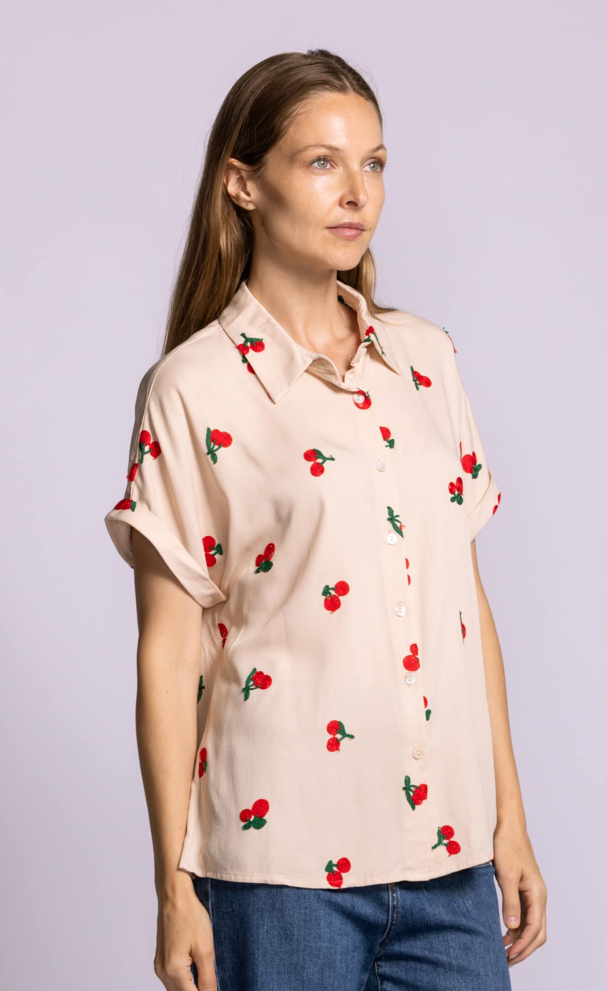 Side angle of Pink Martini Mon Cherry blouse in beige with red cherry embroidery and rolled sleeves.