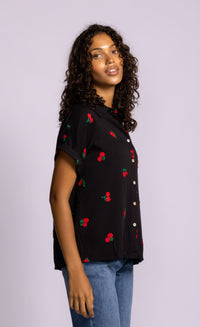 Side angle of Pink Martini Mon Cherry blouse in black with cherry embroidery and rolled sleeves.