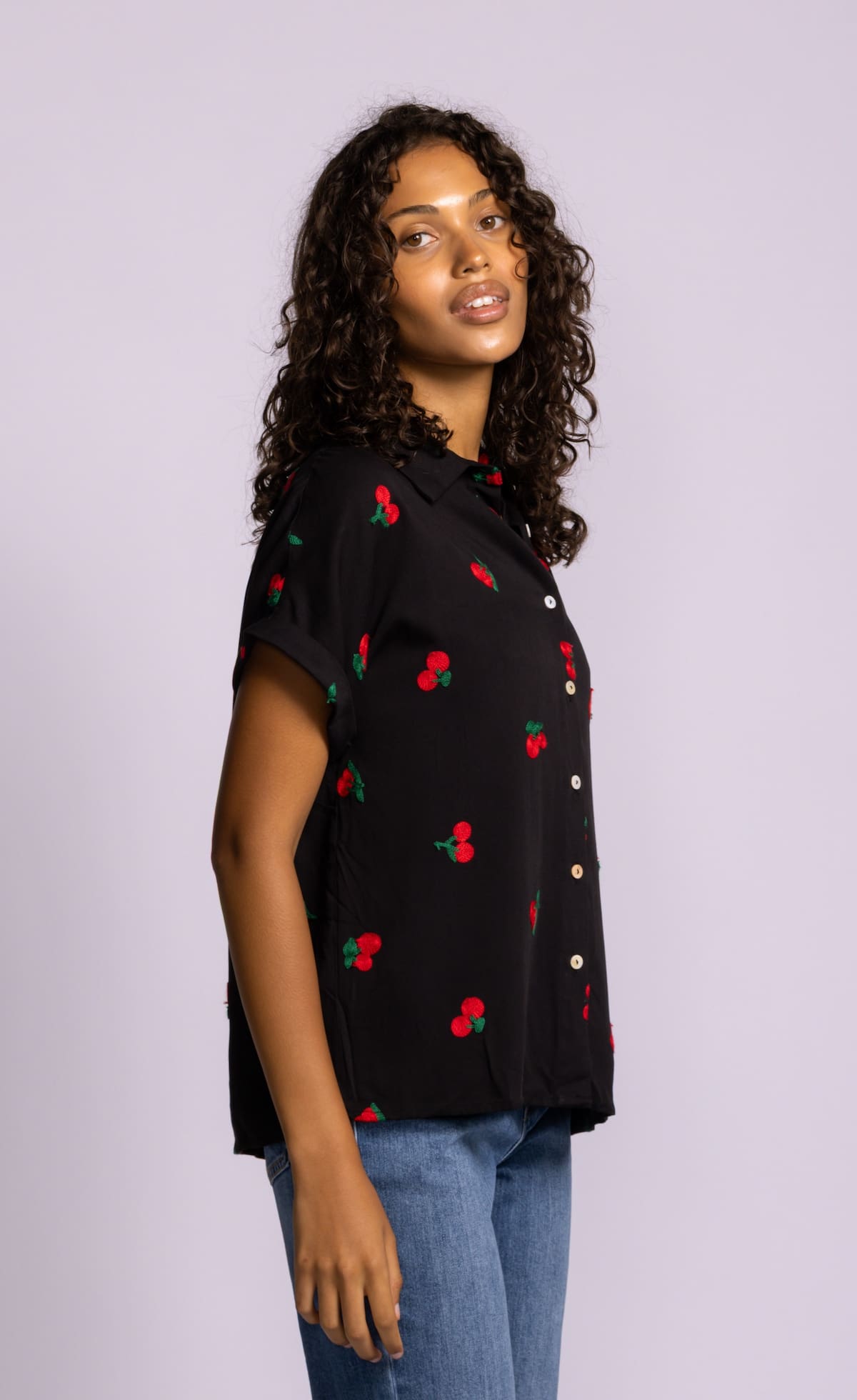 Side angle of Pink Martini Mon Cherry blouse in black with cherry embroidery and rolled sleeves.
