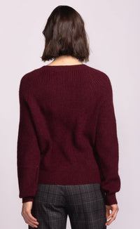 Person wearing a burgundy sweater and plaid pants on a light purple background