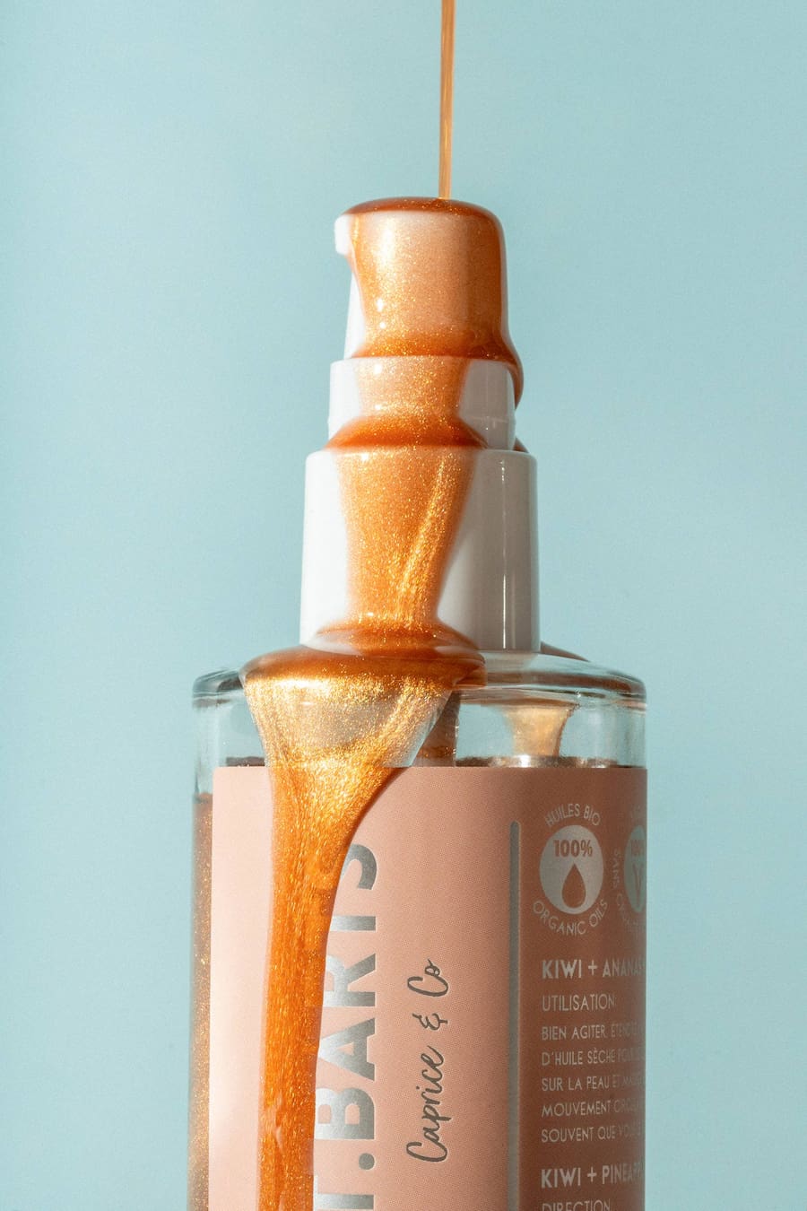 Bronze St. Barts dry shimmering body oil pouring from pump, showing luminous texture and glow.