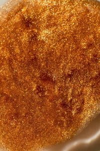Close-up of bronze shimmering body oil texture with fine golden sparkle