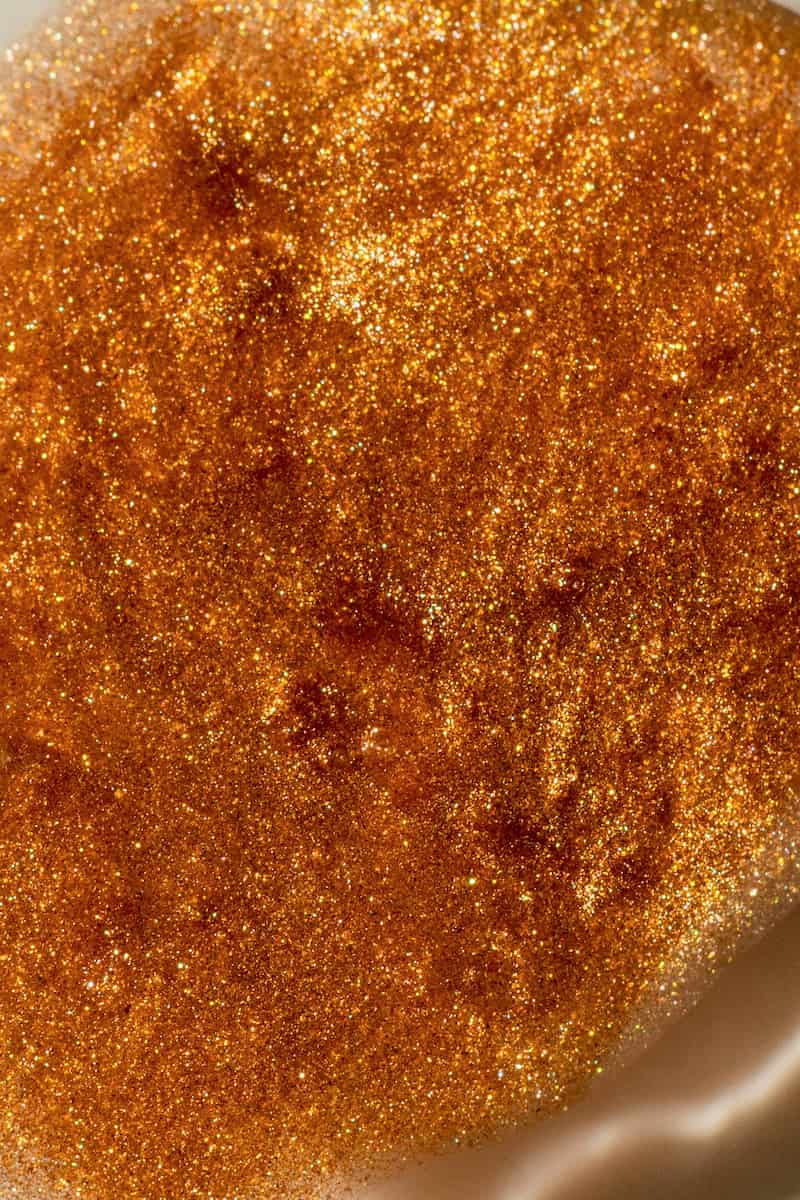 Close-up of bronze shimmering body oil texture with fine golden sparkle