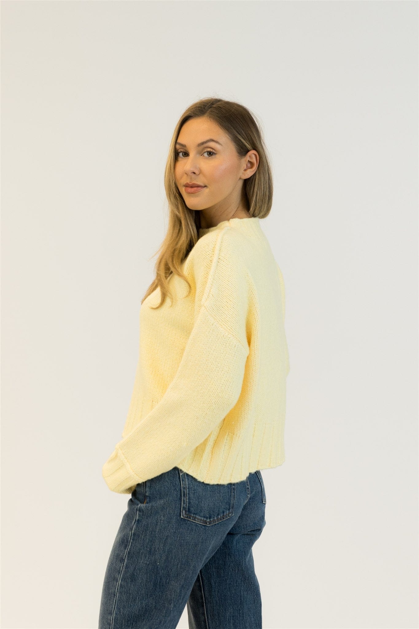 Woman wearing a light yellow sweater and blue jeans on a white background
