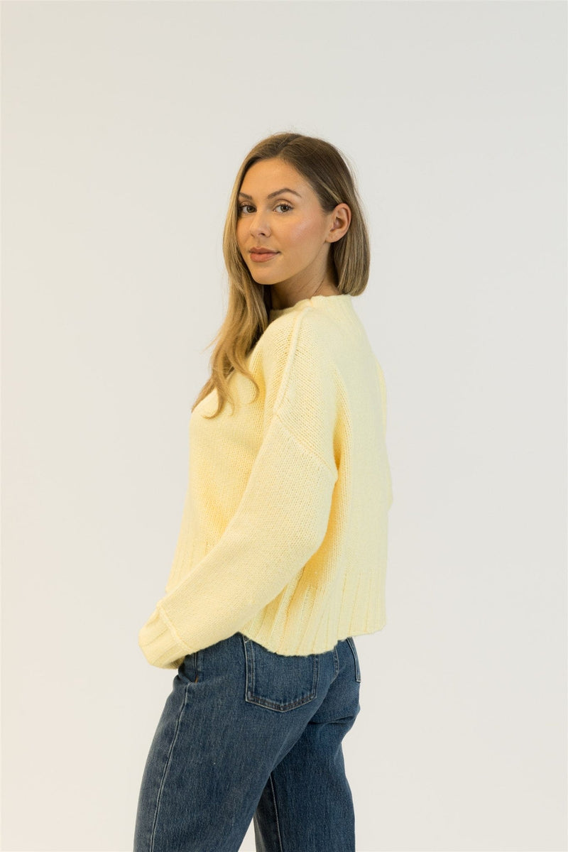 Woman wearing a light yellow sweater and blue jeans on a white background