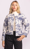 Woman wearing the Toulon Jacket by Pink Martini, front view with blue and cream safari print on padded fabric, styled with black trousers
