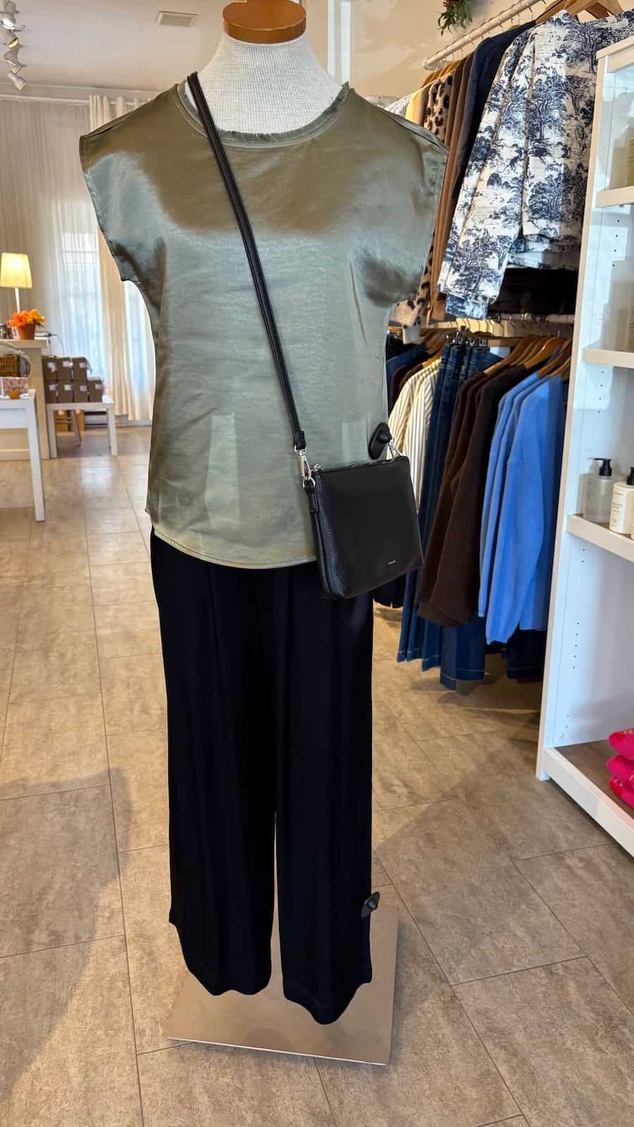 Mannequin wearing a green Willow top by Melissa Nepton and black pants with a crossbody bag inside Lemonberry