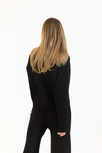 Back view of the black Yassie sweater showing ribbed neckline and soft texture, styled with straight-leg pants.