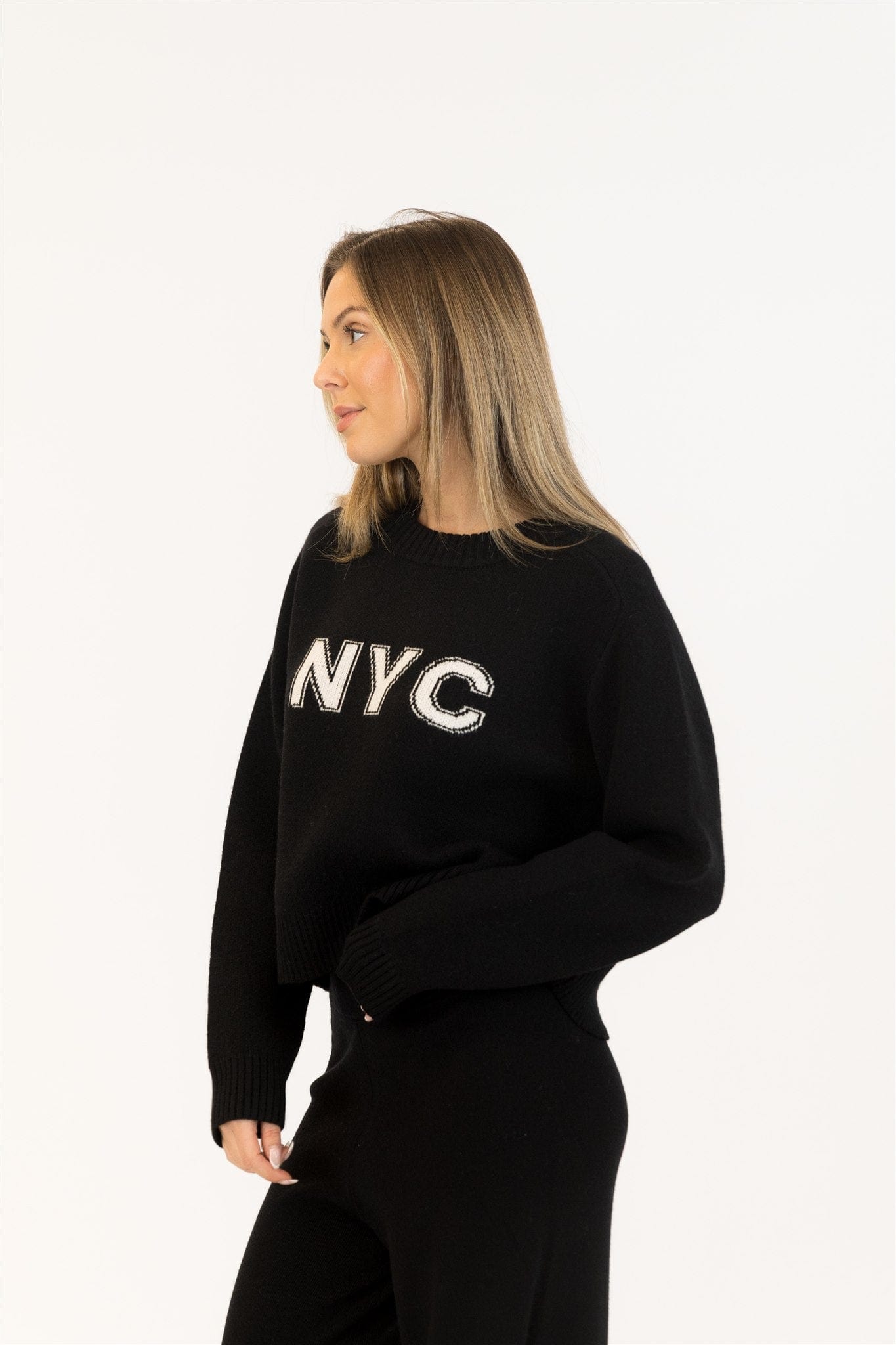 Side view of black Yassie sweater showing relaxed fit and cuffed hem. Casual outfit with minimal styling.