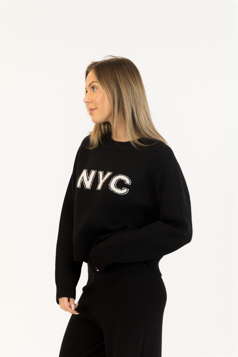 Side view of black Yassie sweater showing relaxed fit and cuffed hem. Casual outfit with minimal styling.